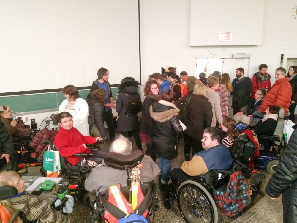 Une foule est réunie dans le bas d'un auditorium. De nombreuses personnes sont en fauteuil roulant.
