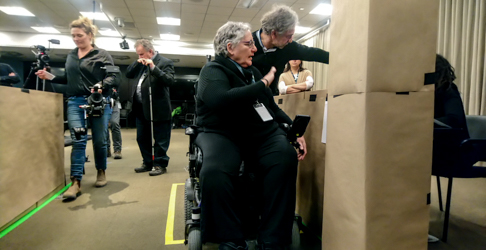 Une femme utilisant un fauteuil motorisé est dans un espace réservé identifié par du ruban au sol. Elle teste la configuration des futurs autobus d'Exo.